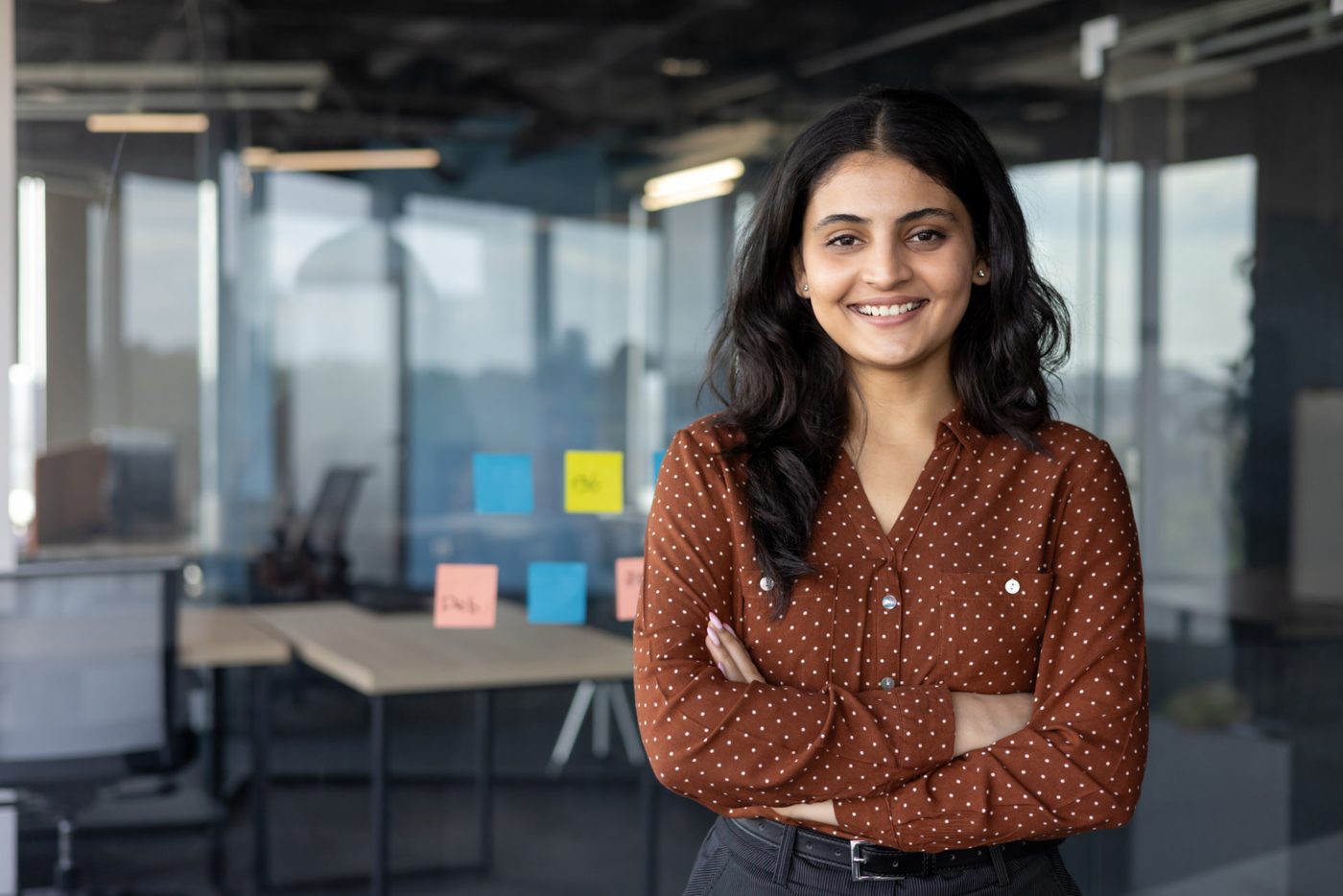 A smiling young woman in a rust-coloured blouse standing in an open-plan office